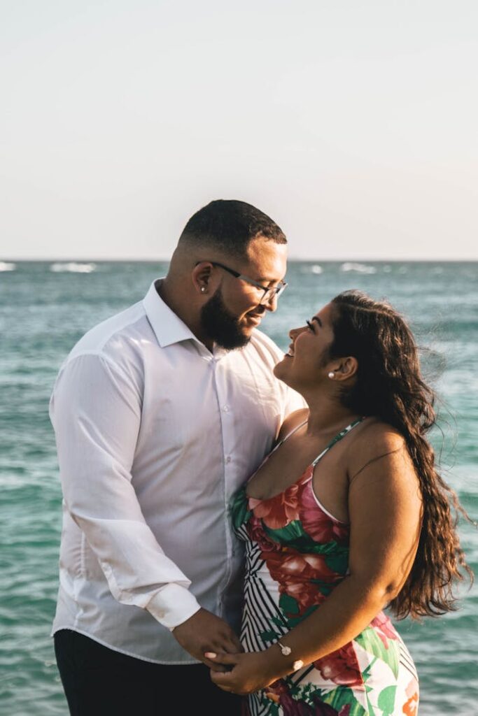 Photo of Happy Couple Looking at Each Other With Ocean in the Background